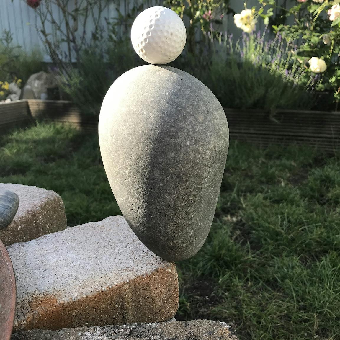 A golf ball is balanced atop a round stone and a brick.